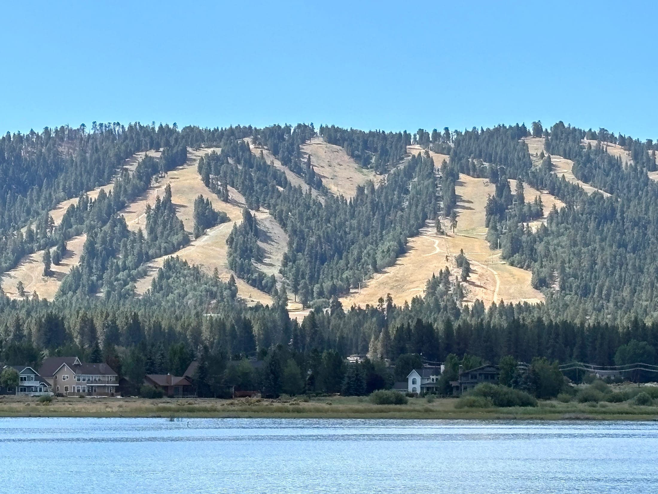Chairlift towers and dry ski runs above homes on the shore of Big Bear Lake