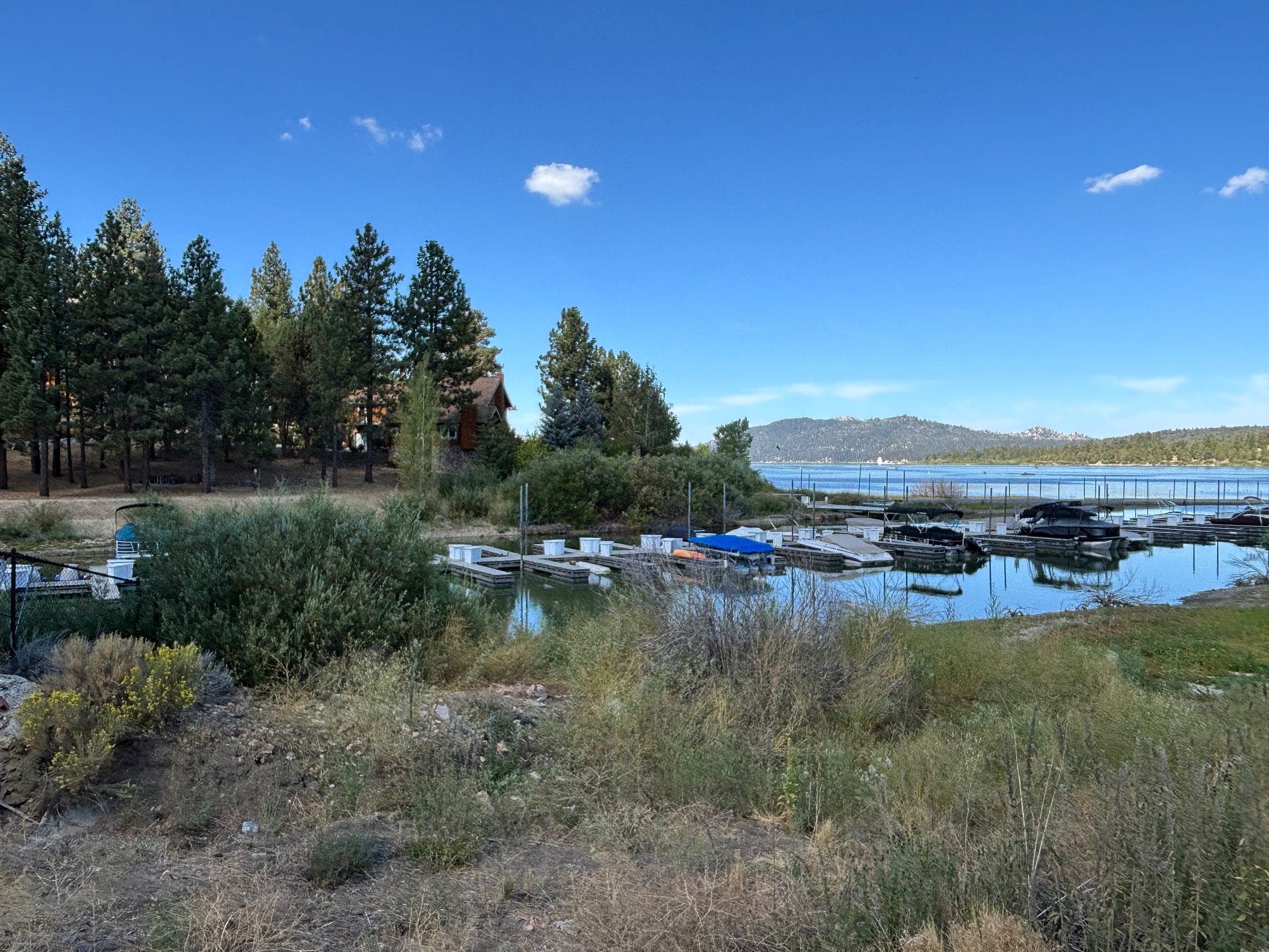 Covered boats at a dock in a Big Bear Lake cove with pines and mountains behind