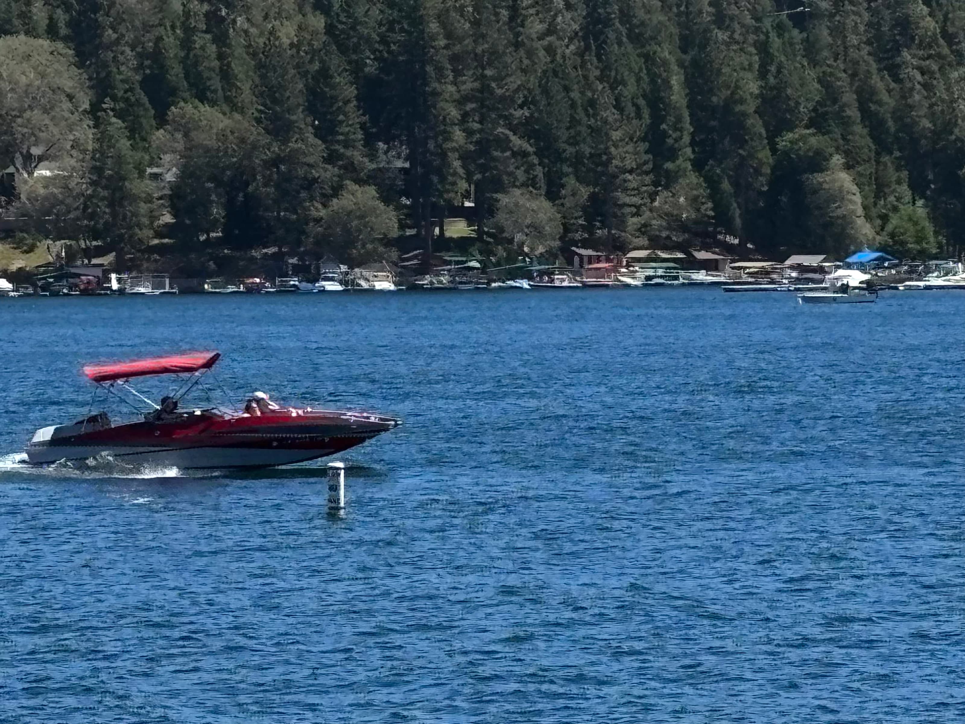 Red motorboat cruising on Lake Arrowhead with forested docks in the background
