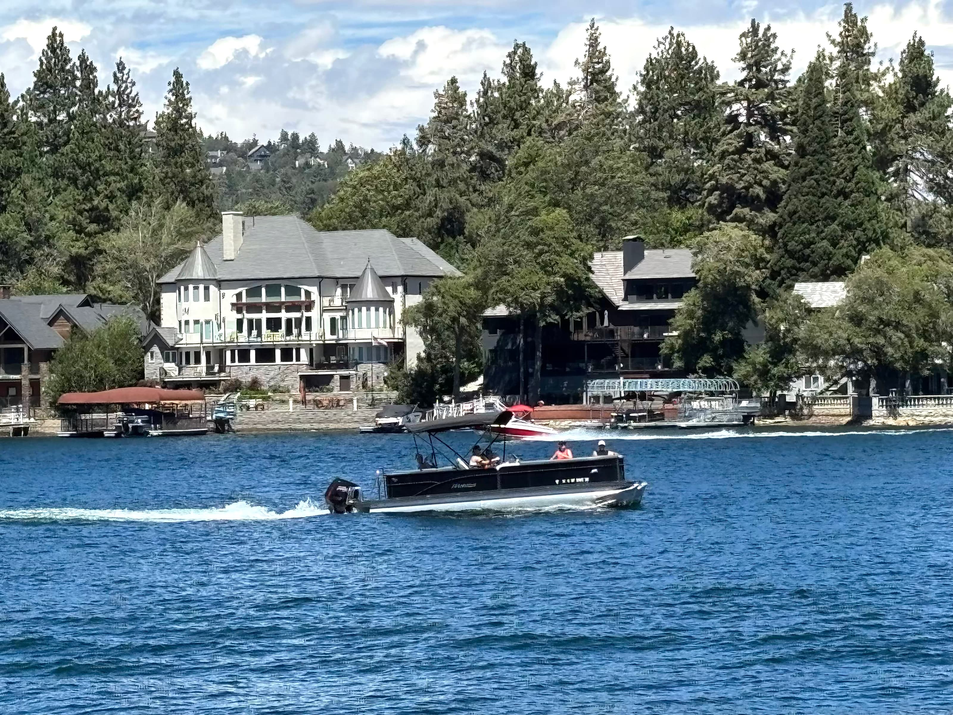 Boats on Lake Arrowhead in front of large waterfront houses among pines.