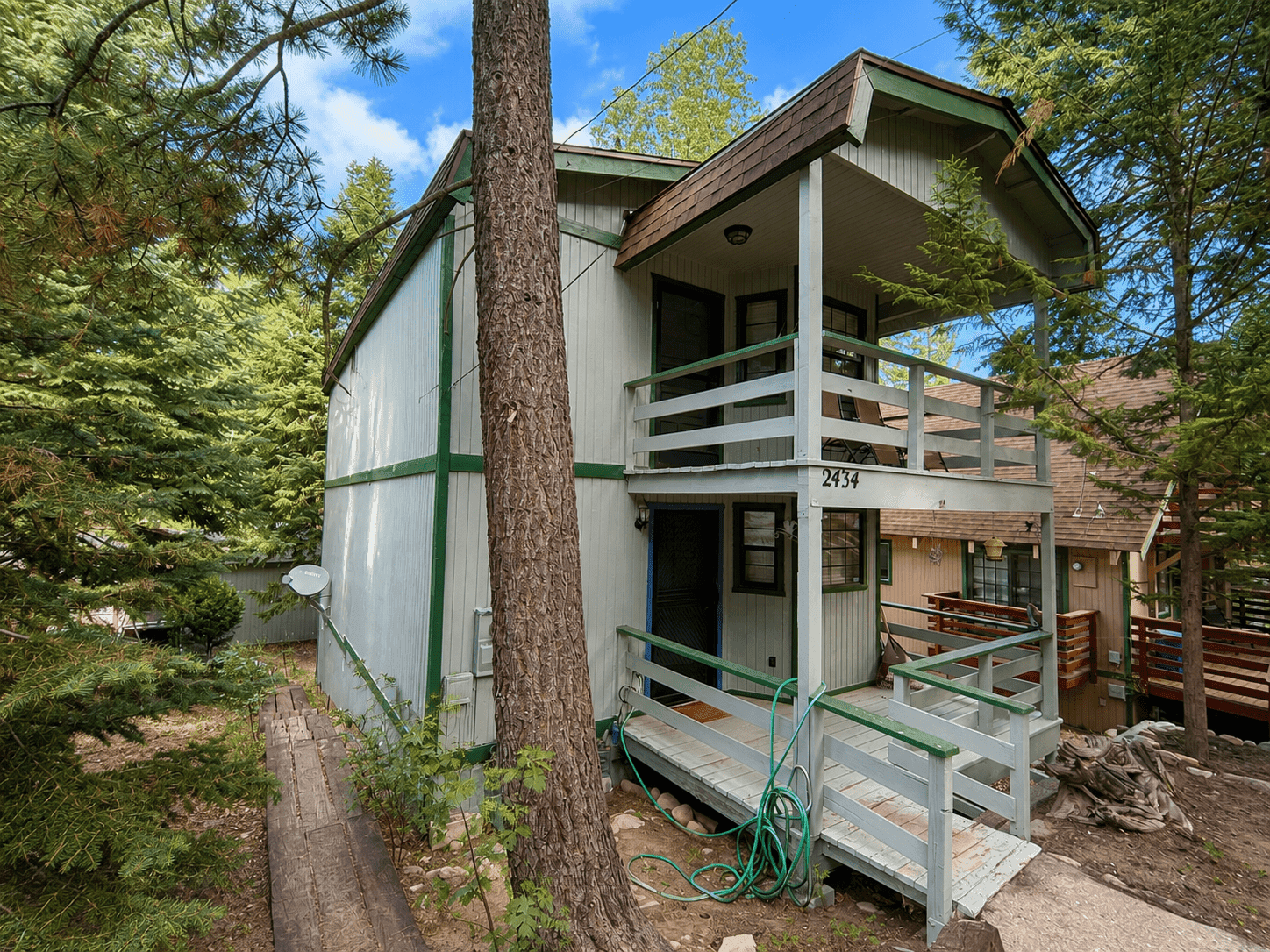 Street view of 2434 Fir Drive showing the house number, wraparound deck, and pines