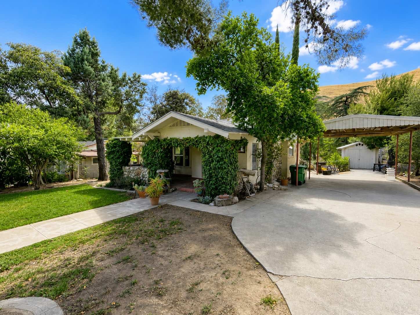 Single-story cottage with an ivy-covered porch, concrete driveway, and white outbuilding at 1951 N San Gorgonio Ave, Banning
