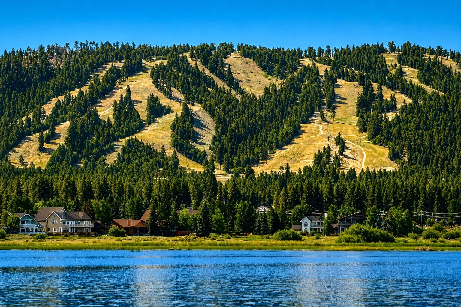 Big Bear Lake shoreline homes with summer ski runs on the forested mountain above