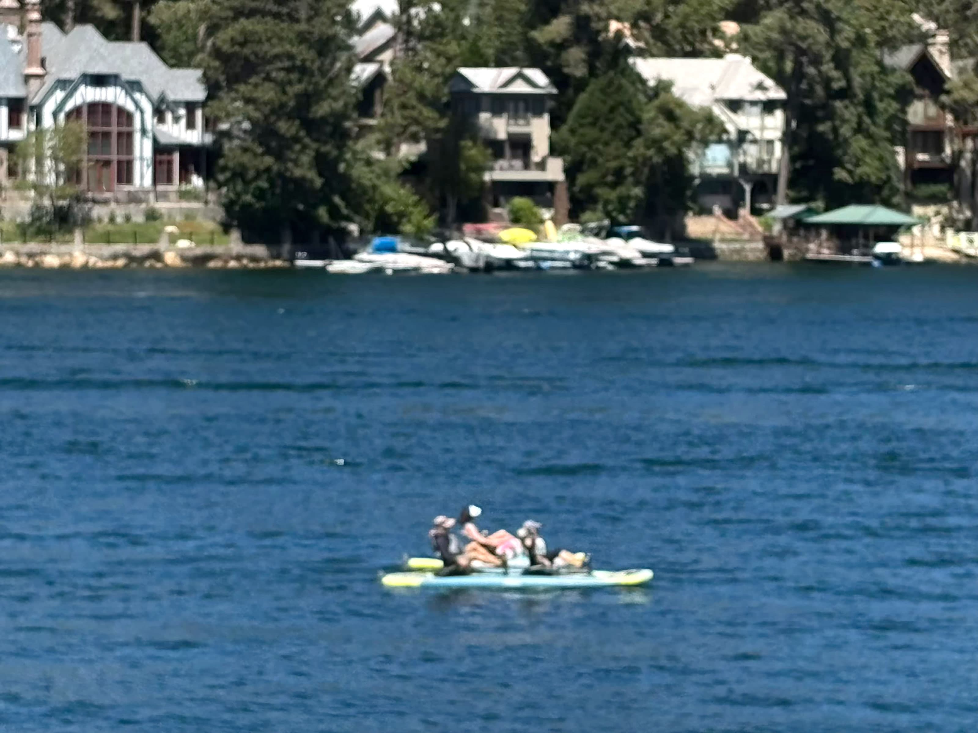 People on an inflatable raft on Lake Arrowhead with shoreline docks and homes.