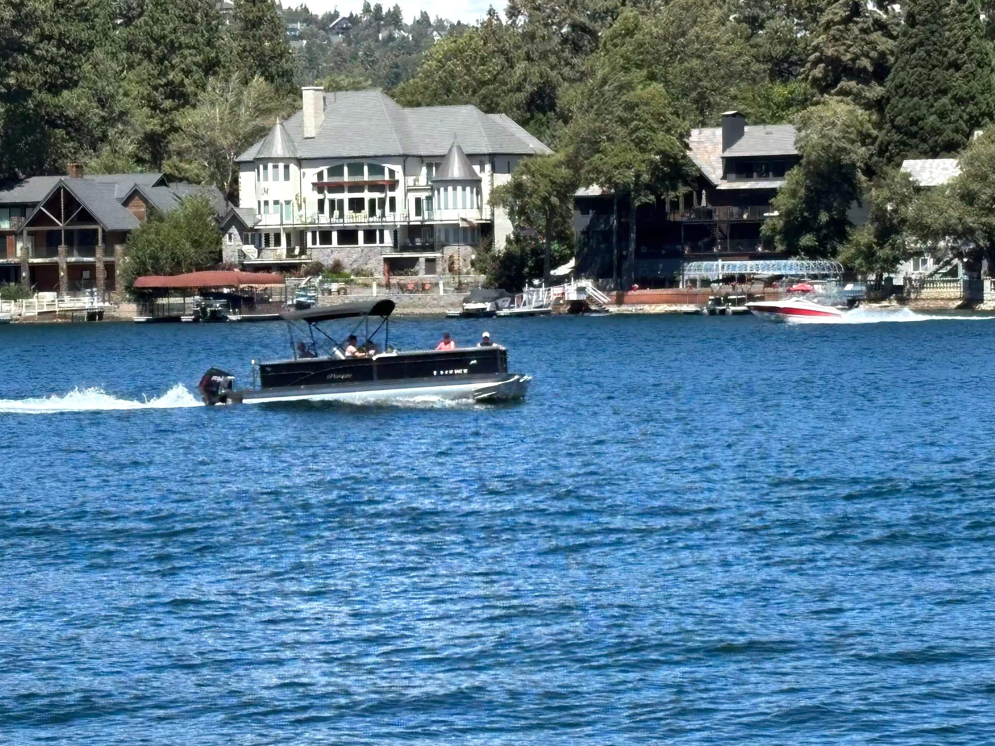 Pontoon boat on Lake Arrowhead with large lakefront homes and docks behind.