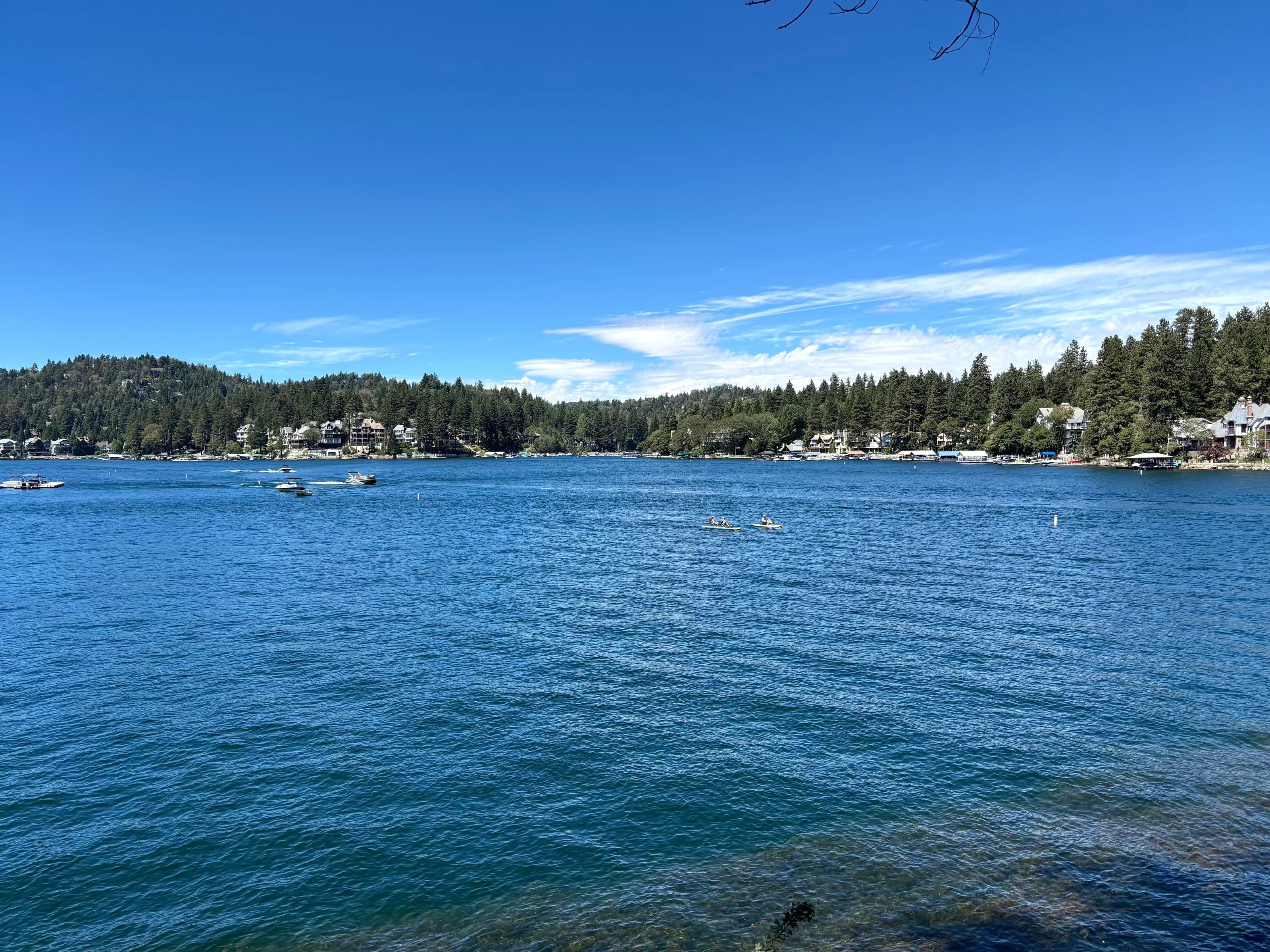 Kayakers on Lake Arrowhead with forested shoreline homes in the distance.