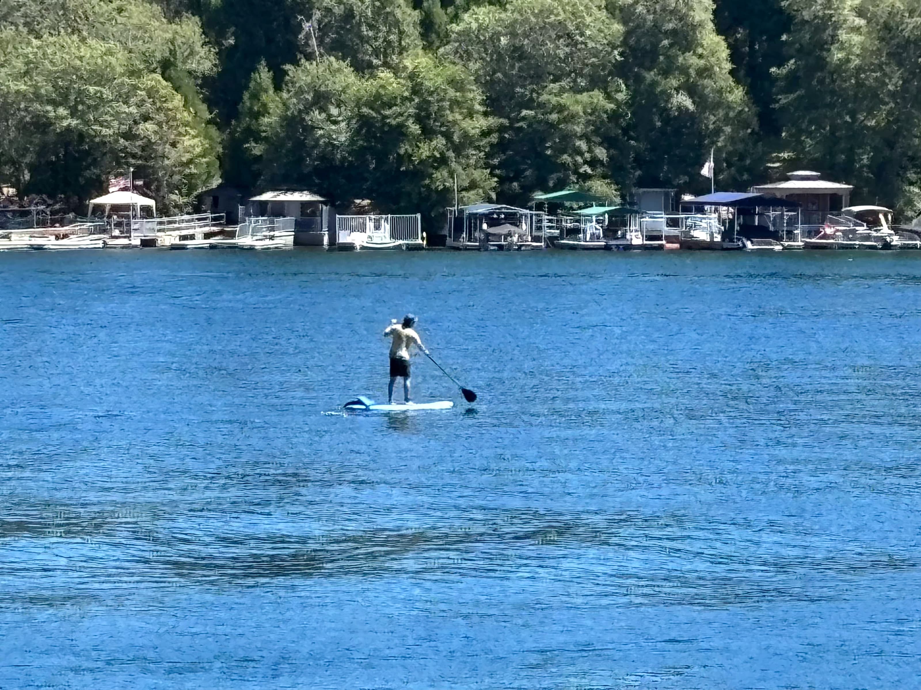 Paddleboarder on Lake Arrowhead facing docks and boathouses along the shore