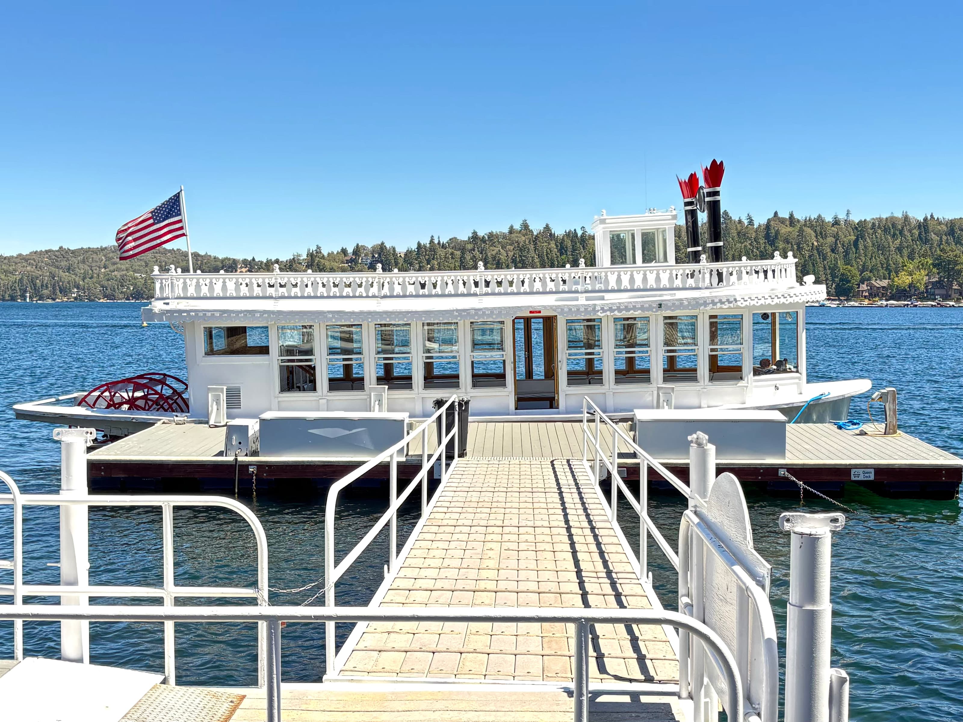 Lake Arrowhead Queen paddlewheeler at a pier with gangway and forested mountains behind