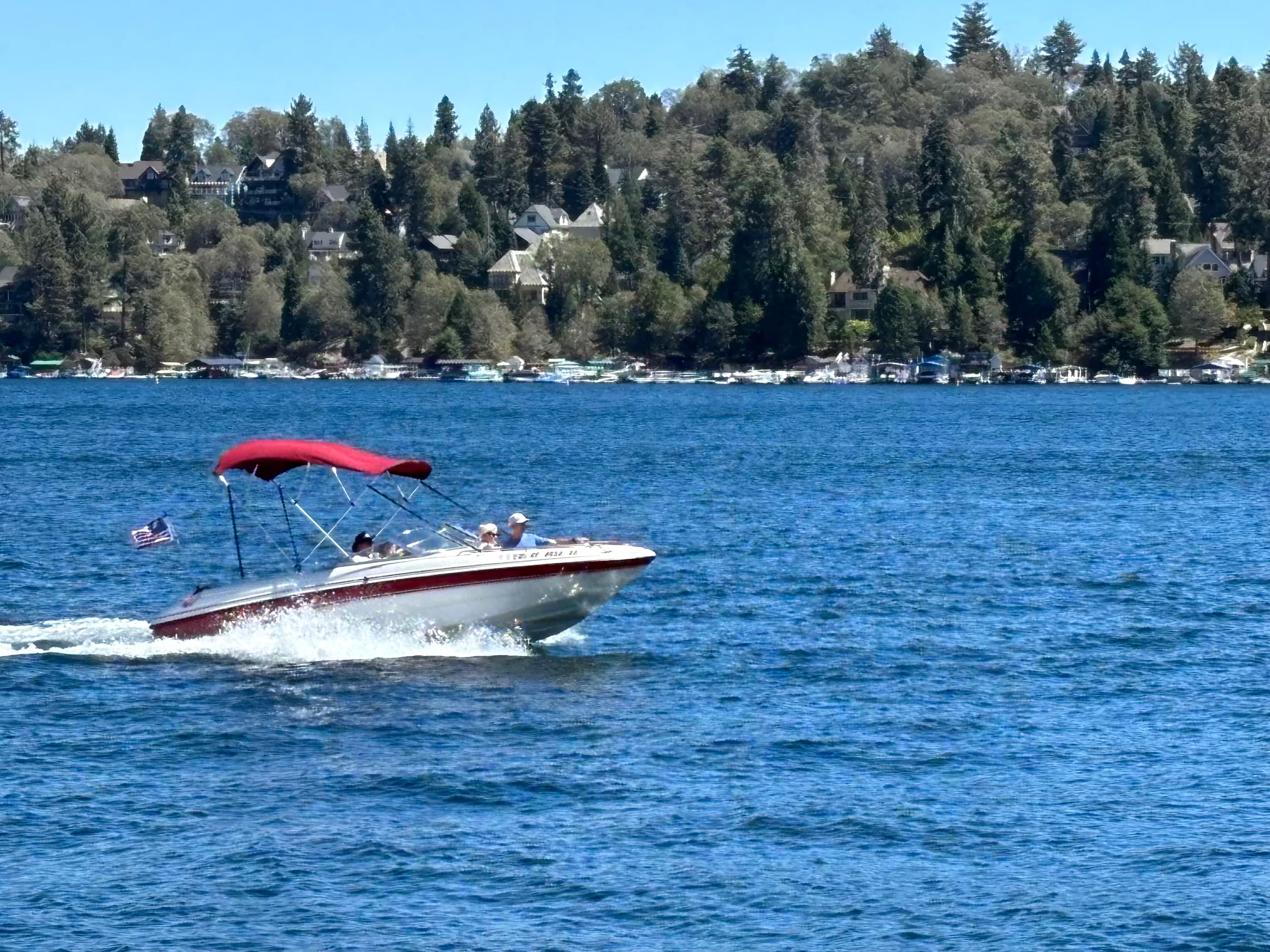 Red and white motorboat on Lake Arrowhead with forested shoreline docks