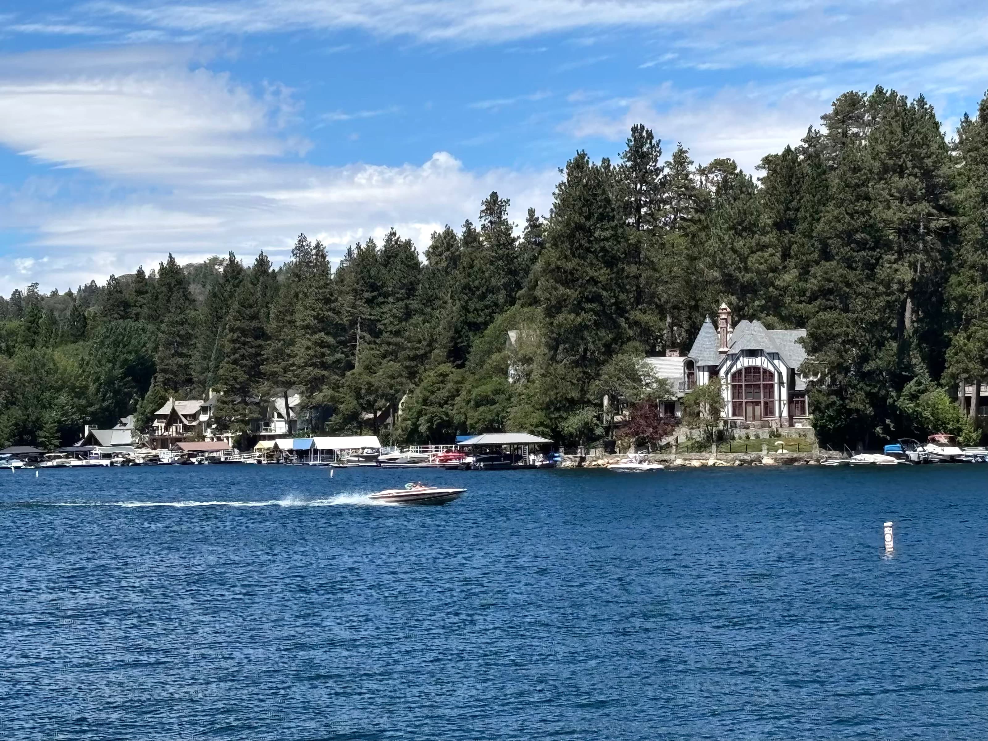 Speedboat on Lake Arrowhead with Tudor-style lakefront homes and pines behind.