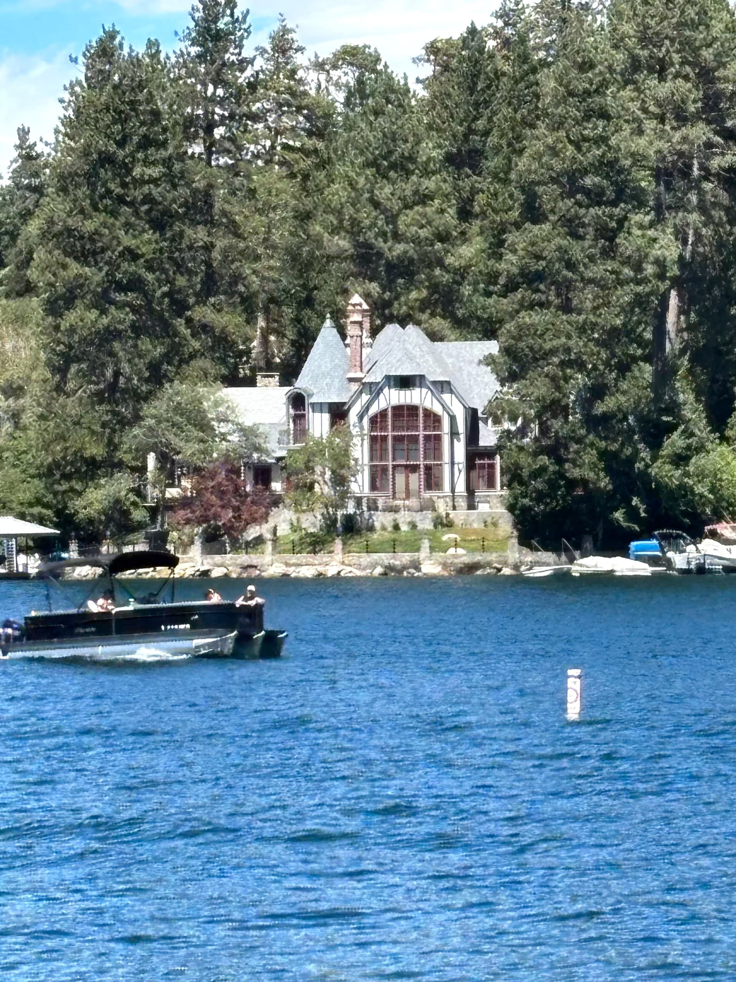 Pontoon boat passing a Tudor lakefront house on Lake Arrowhead.