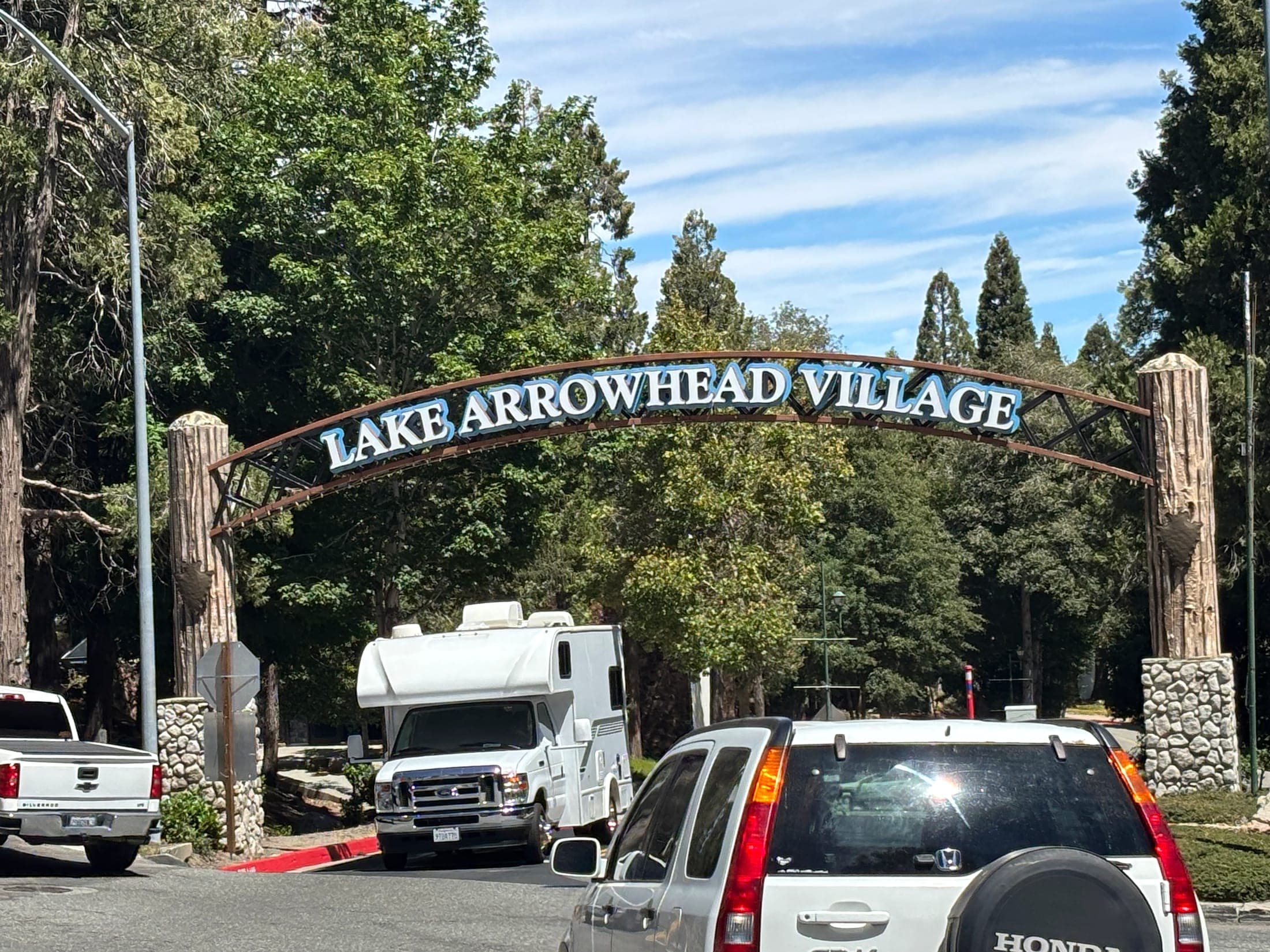Lake Arrowhead Village entrance arch over a mountain road with pine trees behind it