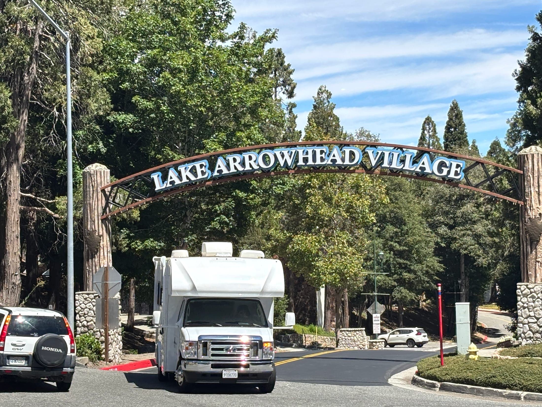 Vehicle driving under the Lake Arrowhead Village gateway surrounded by forest