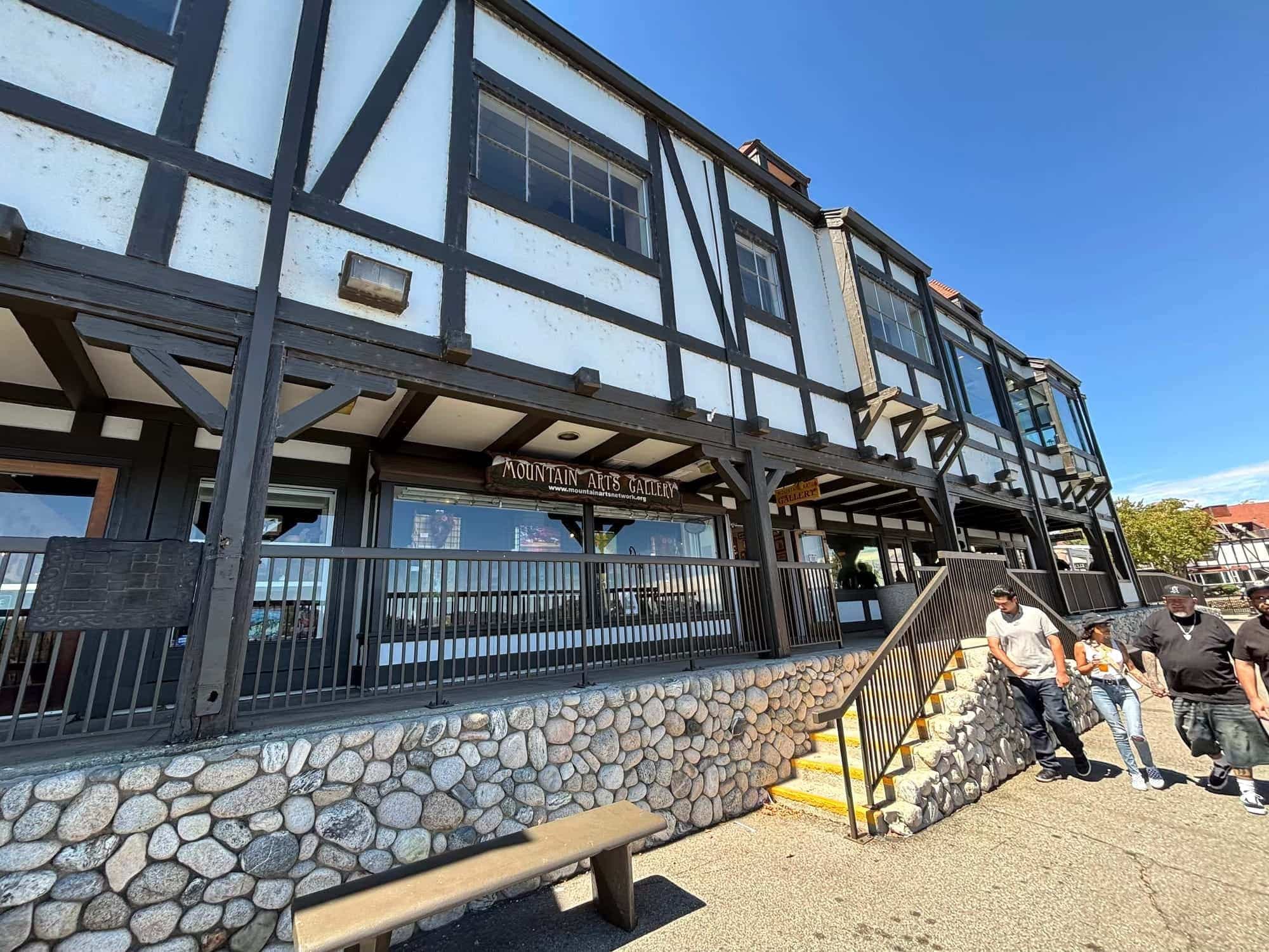 Tudor-style Lake Arrowhead Village building with stone base and Mountain Arts Network gallery sign