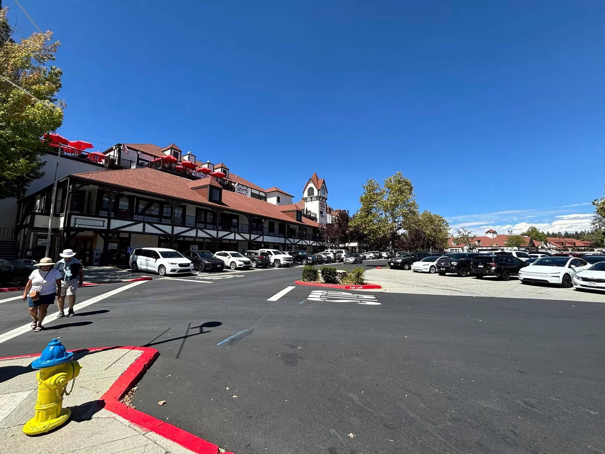 Lake Arrowhead Village Tudor-style shops, parking lot, and red umbrellas on a sunny day