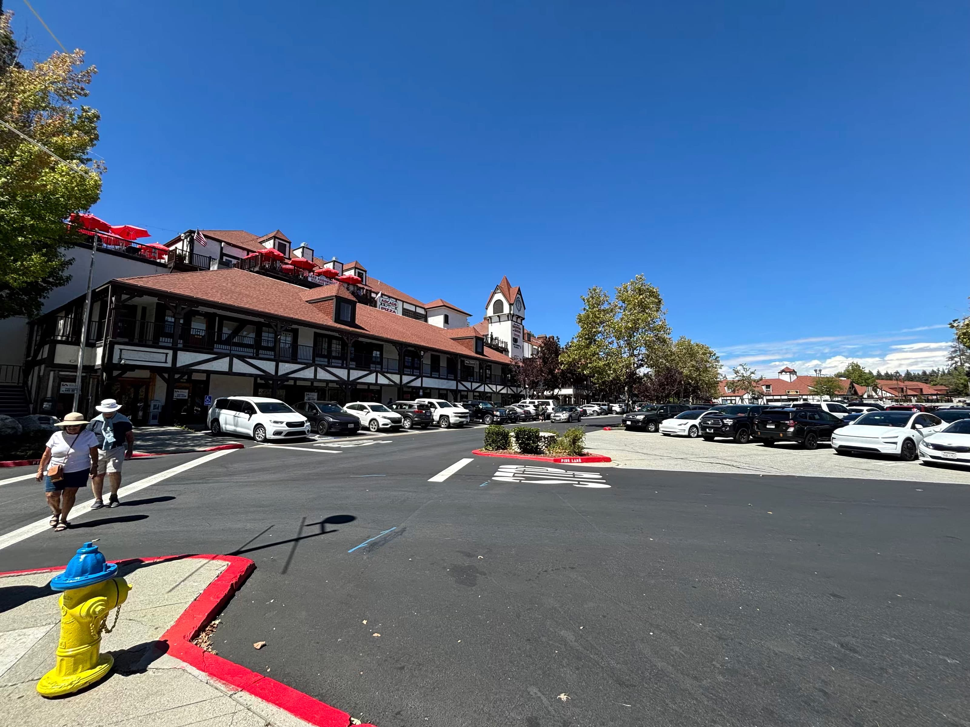 Lake Arrowhead Village Tudor-style shops, parking lot, and red umbrellas on a sunny day