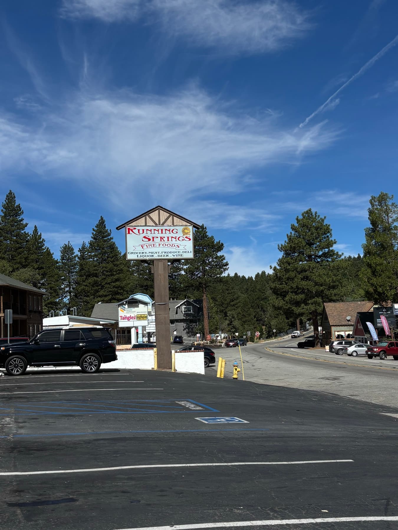 Running Springs Fine Foods grocery sign beside a parking lot and pine trees