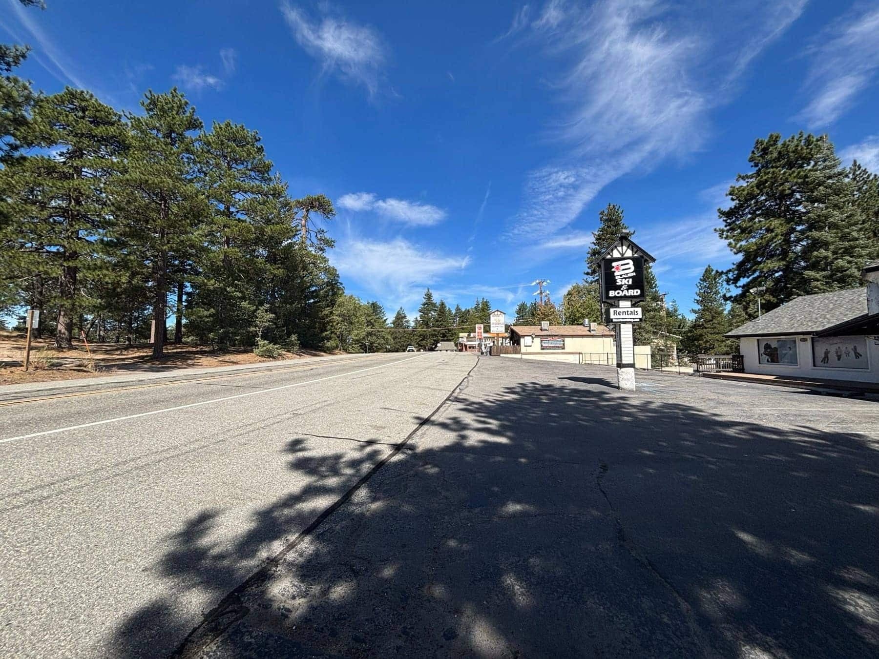 Paved mountain road in Running Springs with pine trees and a ski and snowboard rental shop