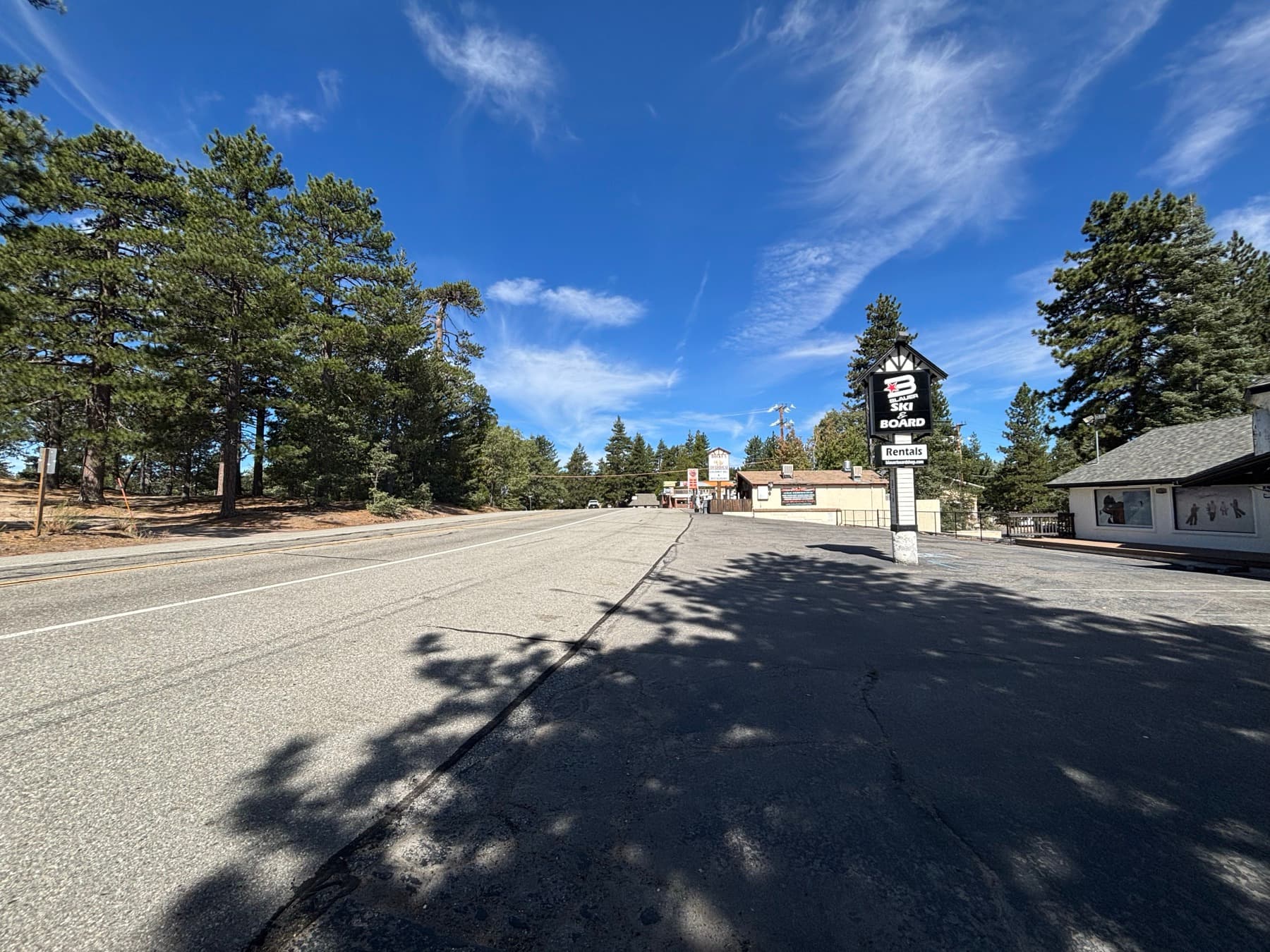 Paved mountain road in Running Springs with pine trees and a ski and snowboard rental shop