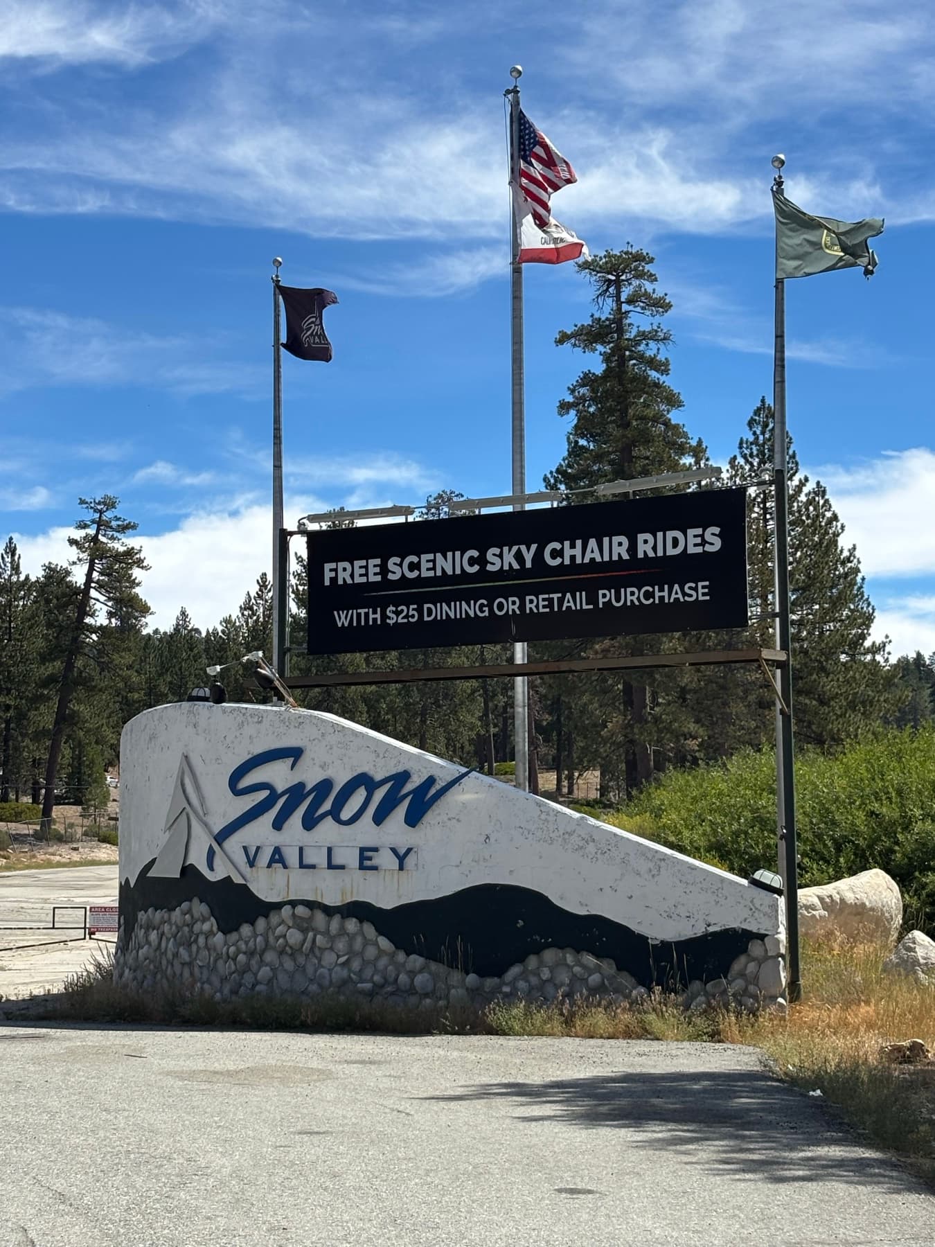 Snow Valley Mountain Resort entrance sign with flags and pine forest