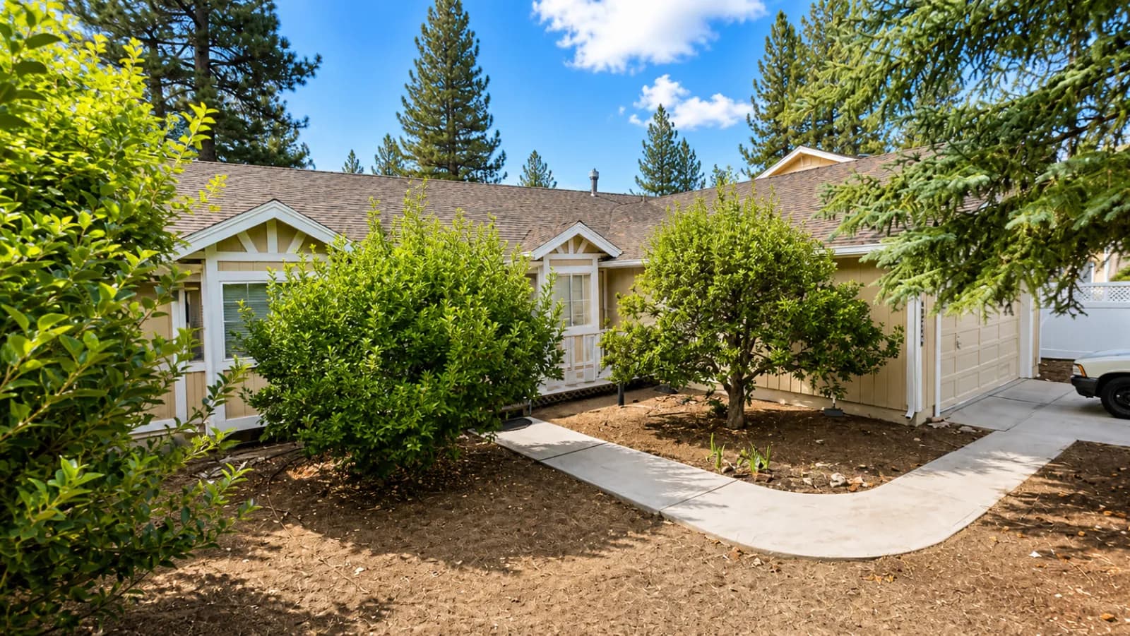 Front of a tan single-story house with white trim, shrubs, and a curving walkway to the door and garage.